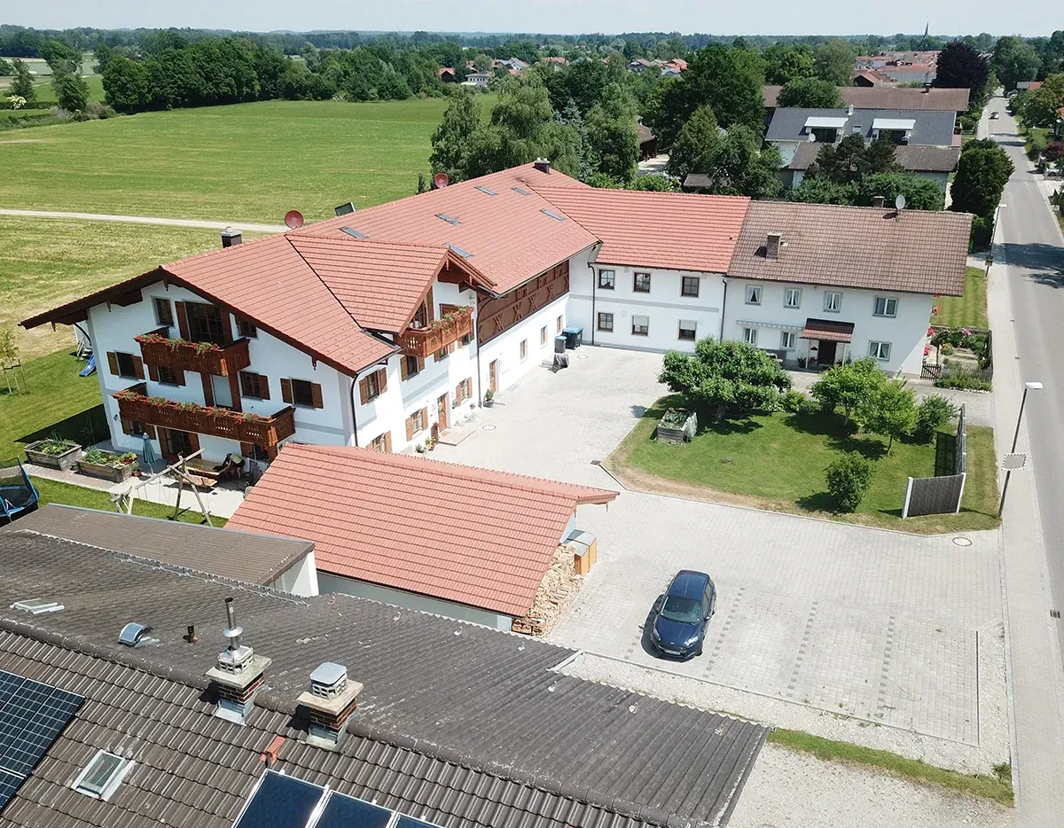 Luftaufnahme eines Gebäudekomplexes mit roten Dächern und weißen Fassaden neben einem Kieshof und grünen Feldern