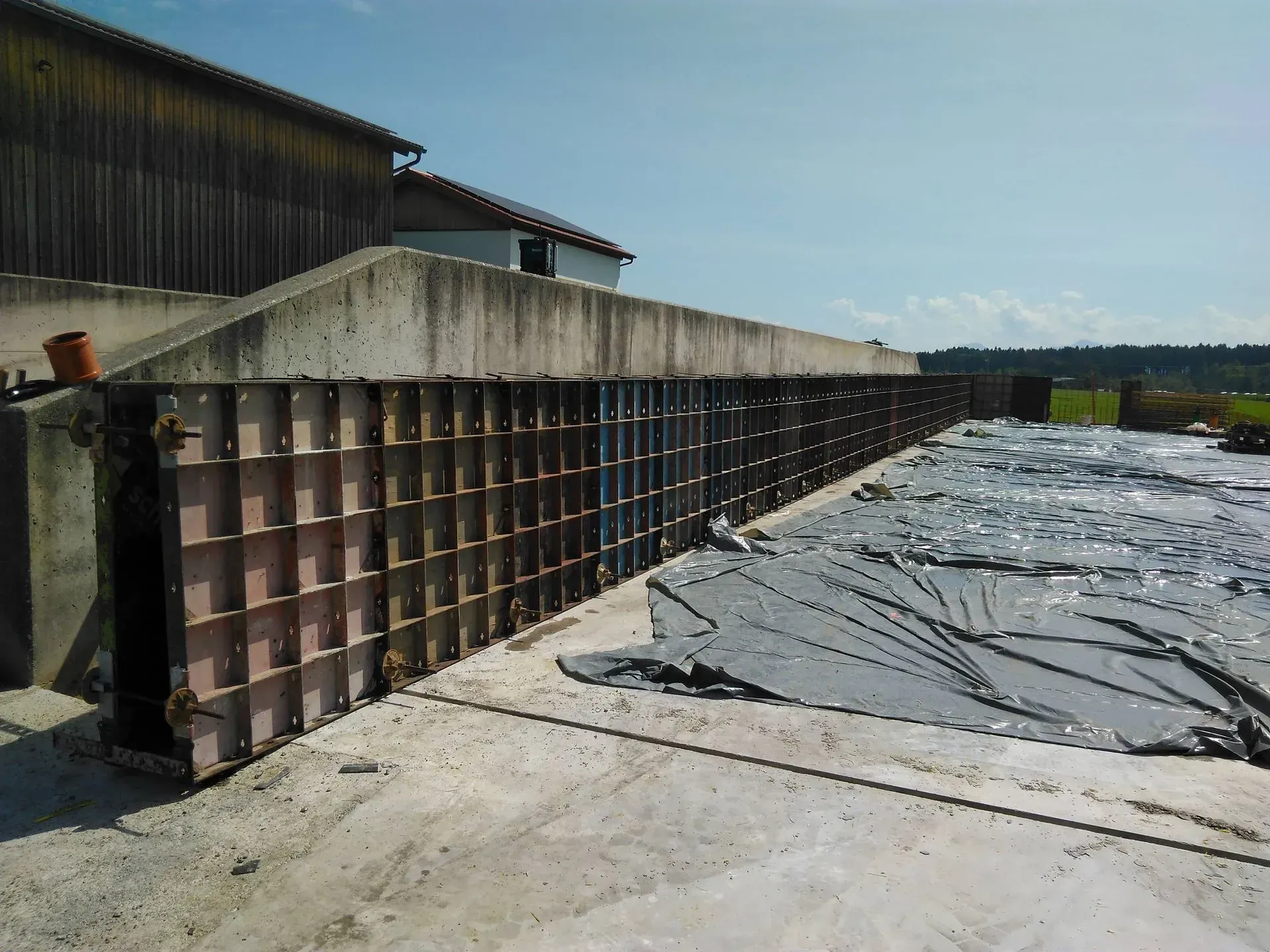 Industriegelände im Freien mit Betonbarriere neben einem Gebäude und abgedeckten Bodenplanen