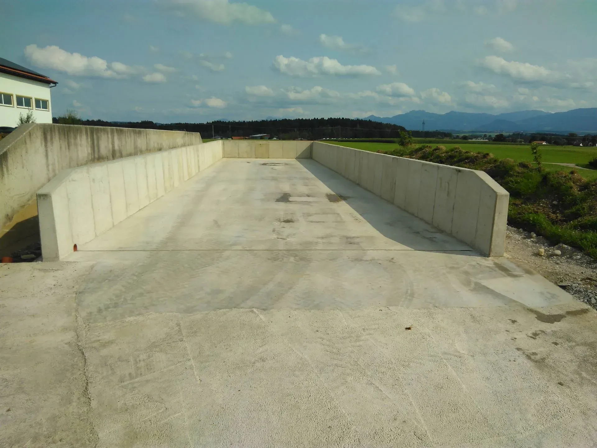 Im Bau befindliche Betonbrückenfahrbahn, flankiert von niedrigen Stützmauern in ländlicher Umgebung.