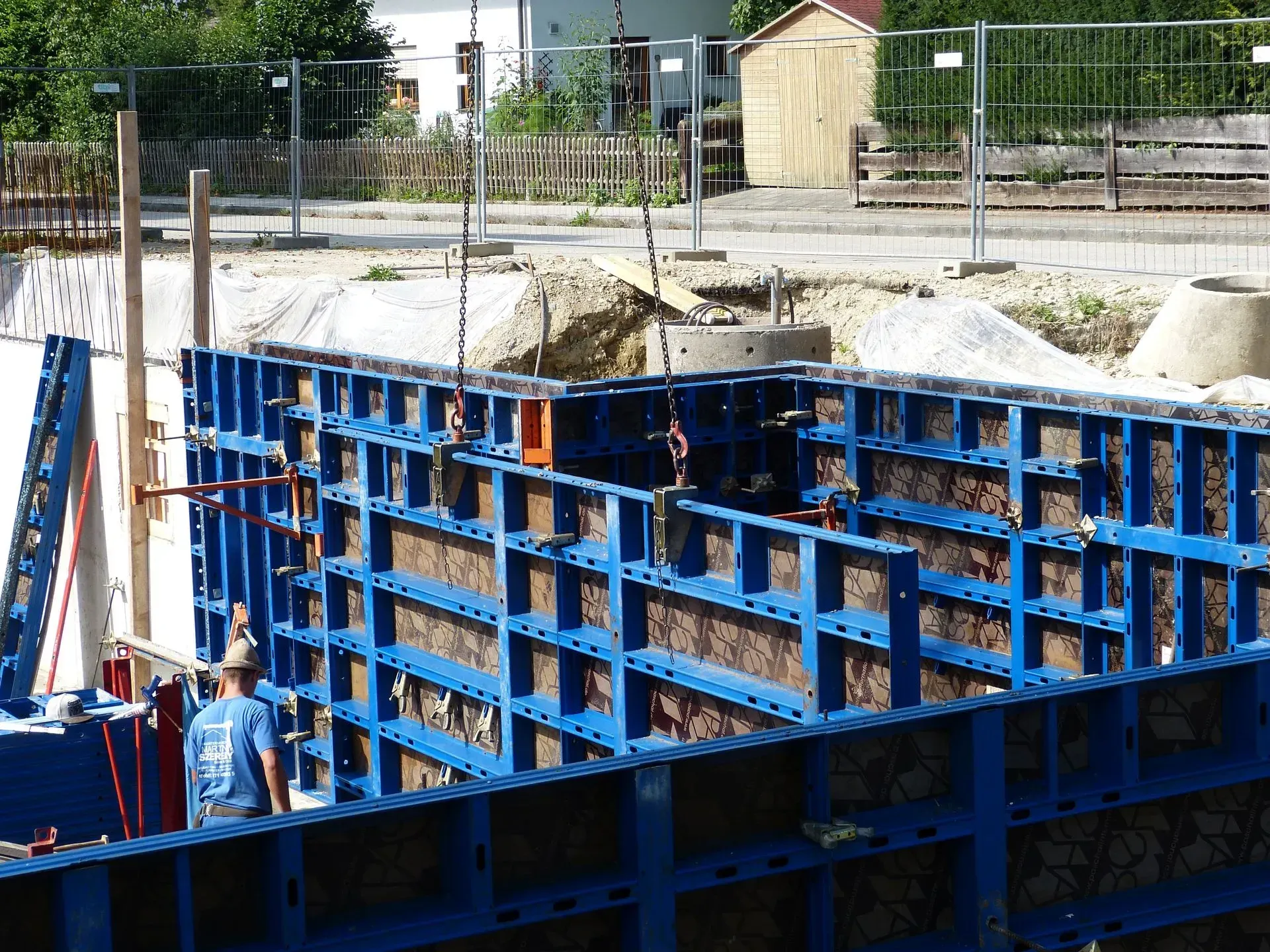 Blaue Stahlschalung auf einer Baustelle, darunter Arbeiter und im Hintergrund ein eingezäuntes Gelände.