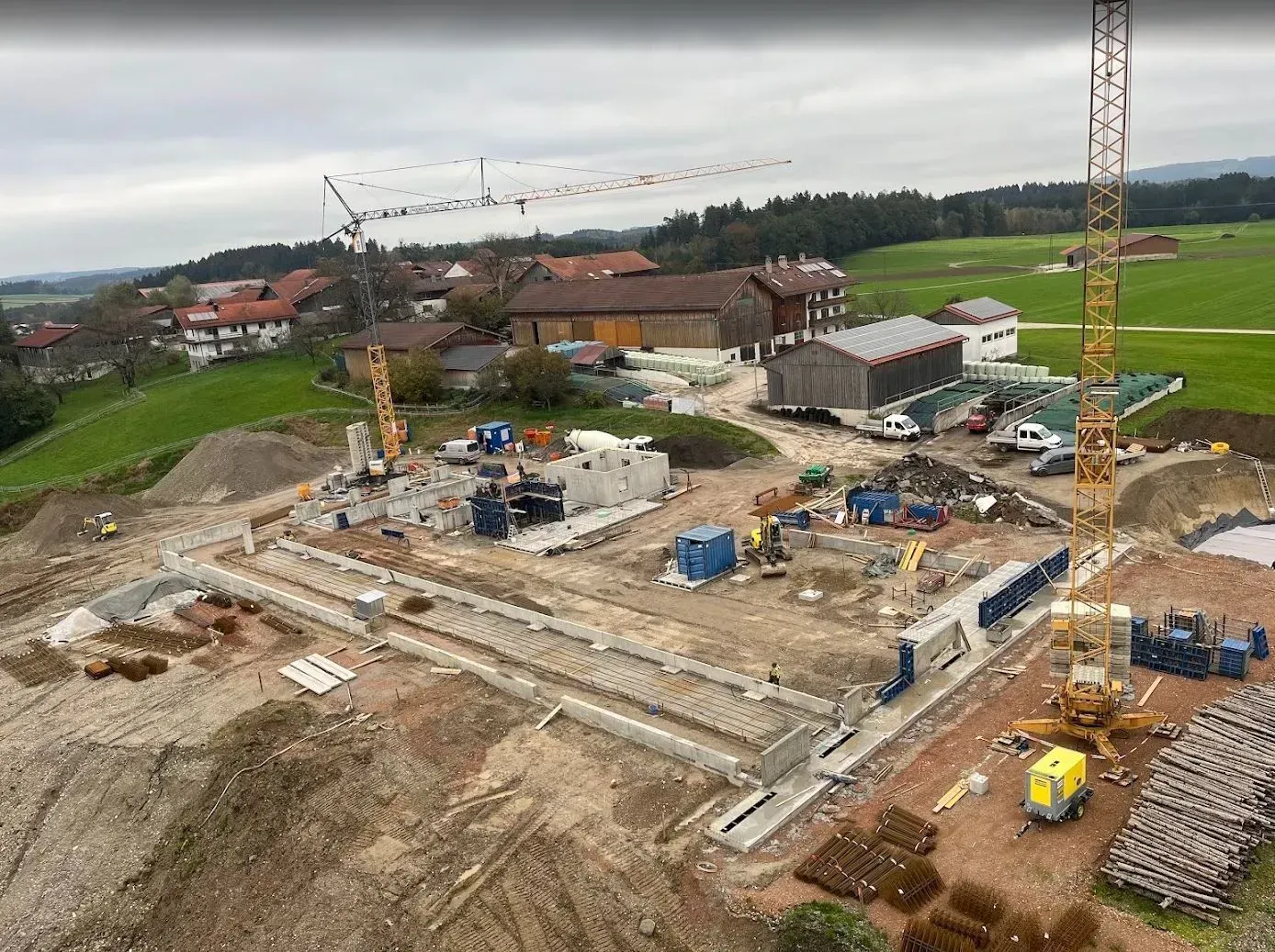 Baustelle mit Kränen und Betonfundamenten in der Nähe von Feldern und Häusern