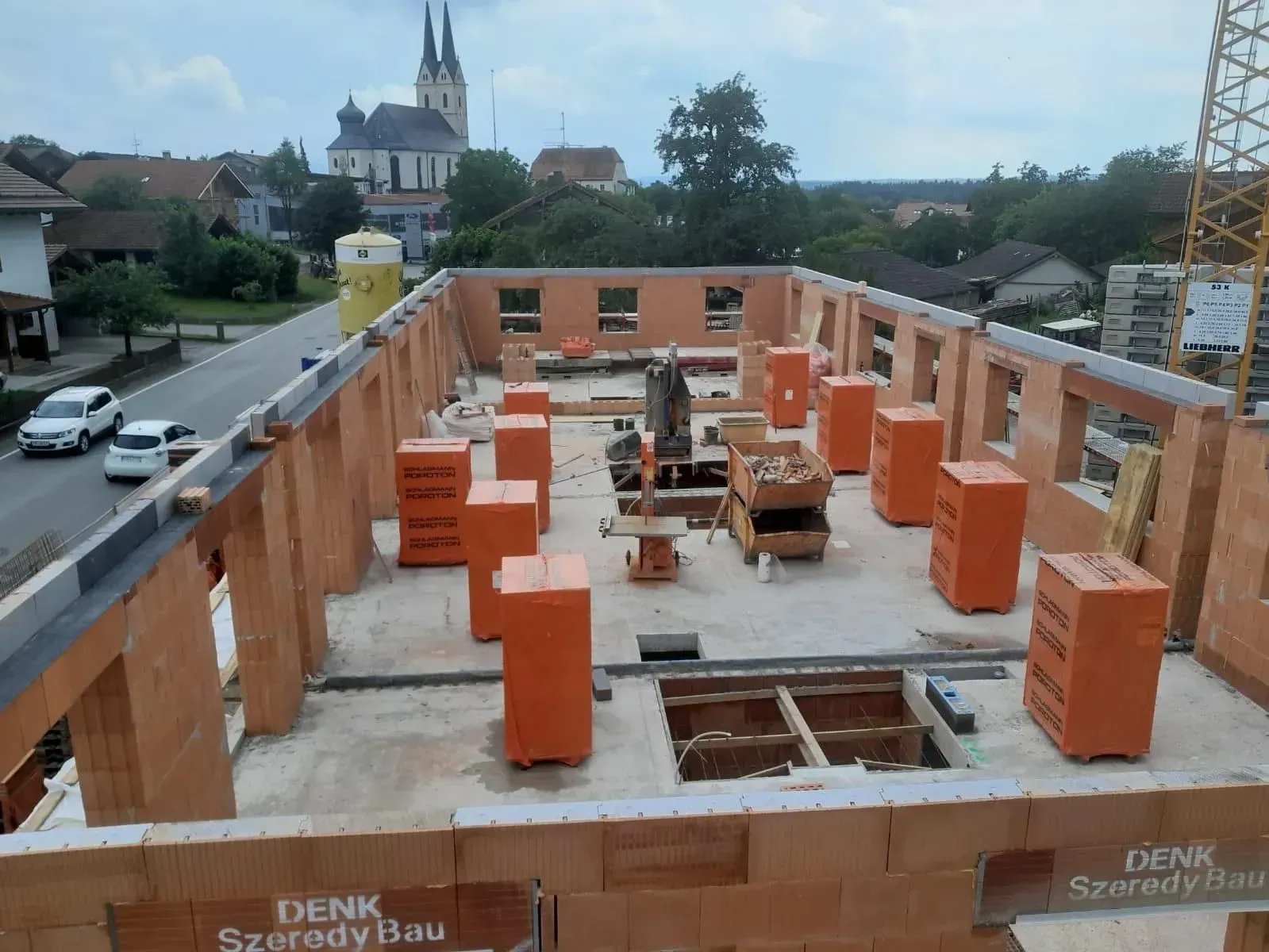 Baustelle mit Ziegelwänden und orangefarbenen Dämmblöcken auf einem Hausdachstuhl.