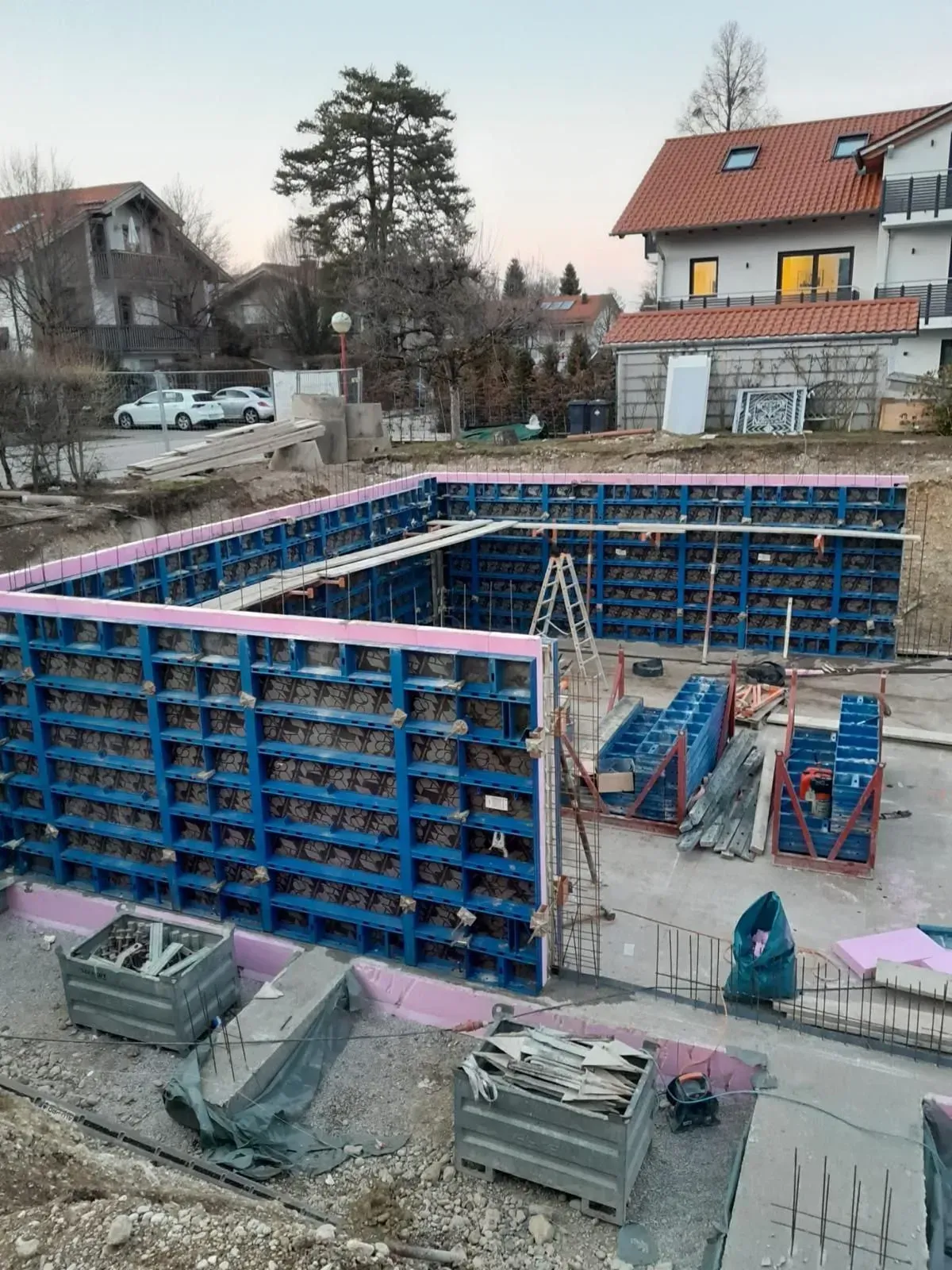 Baustelle mit einer großen rechteckigen Fundamentschalung und gestapelten Materialien neben Häusern