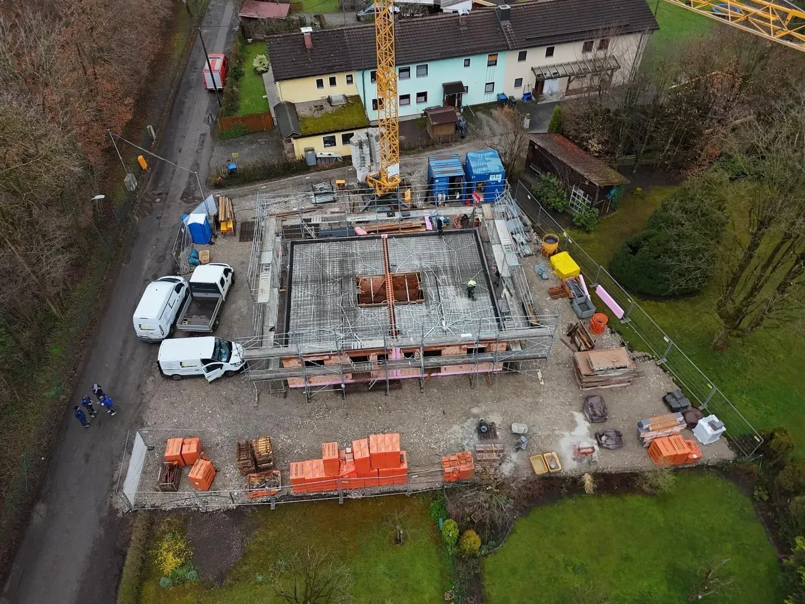Luftaufnahme einer Hausbaustelle mit Betonfundament, Lastwagen und Baumaterialien.