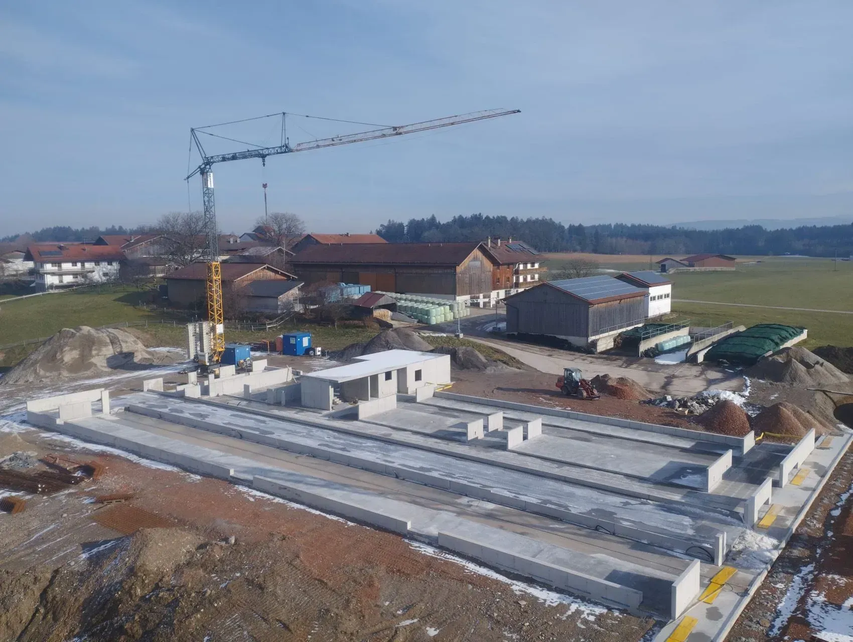 Baustelle mit Betonfundamentplatten, einem Kran und Gebäuden im Hintergrund