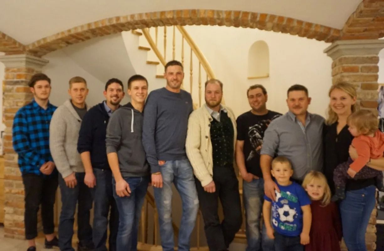 Eine Gruppe von Menschen posiert drinnen unter einem Backsteinbogen, im Vordergrund stehen zwei Kinder.