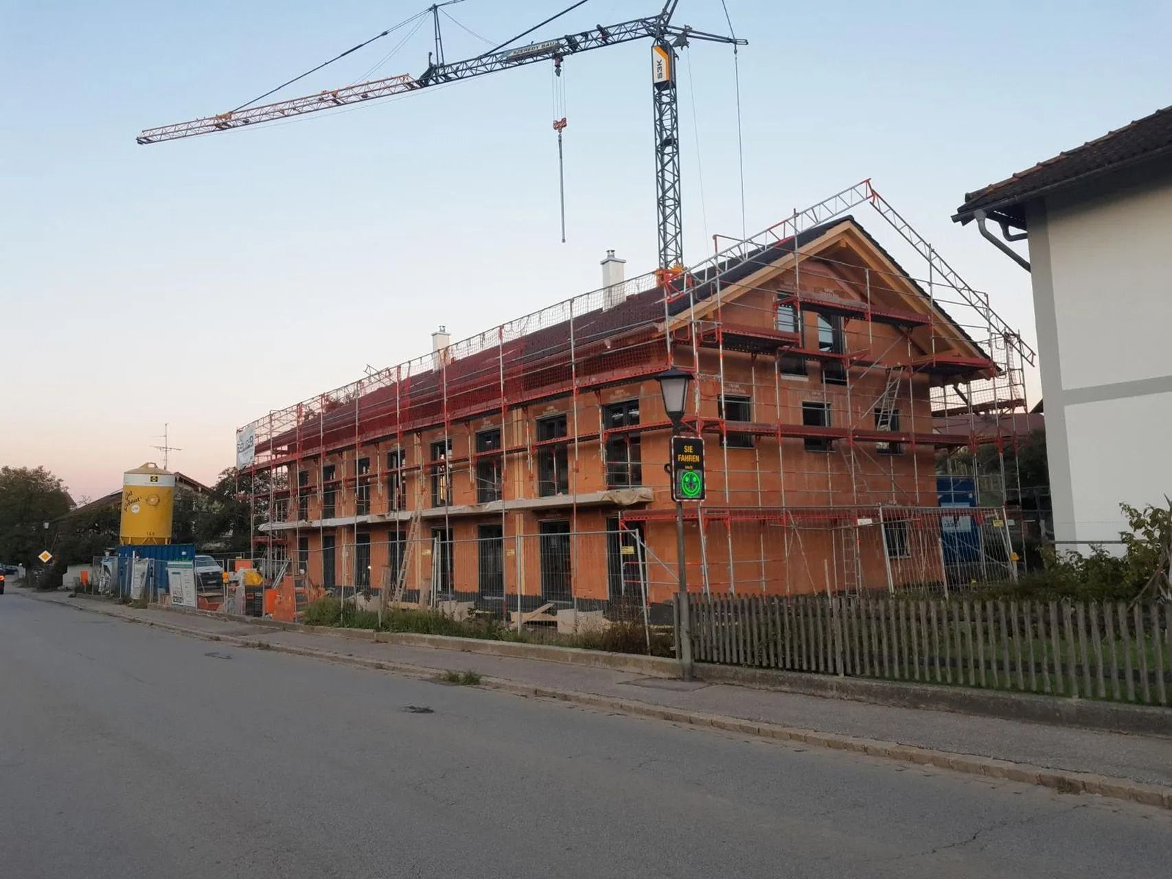 Backsteingebäude im Bau mit Gerüst und Kran neben einer Straße in der Abenddämmerung