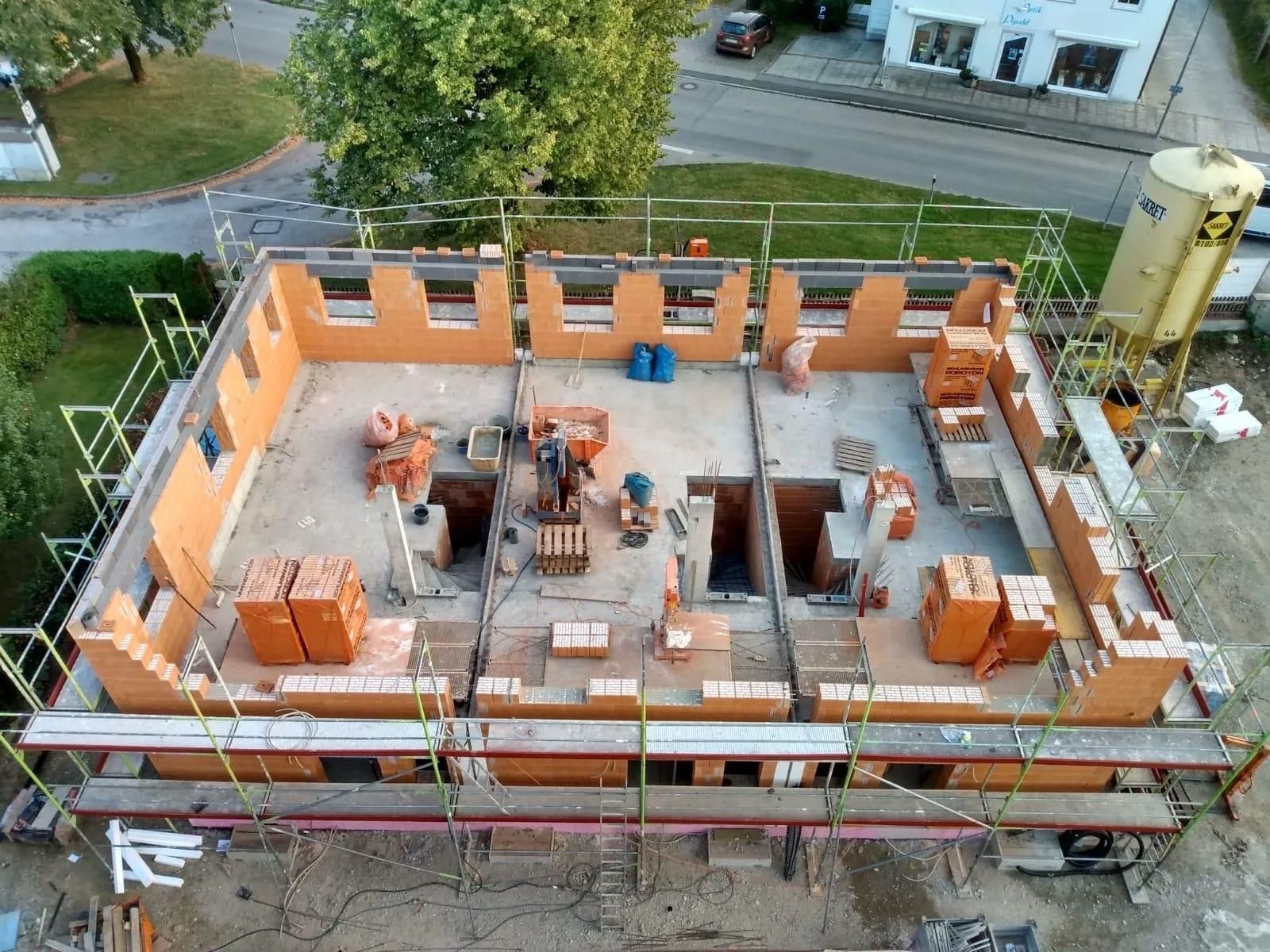 Baustelle mit orangefarbenen Wänden und Gerüsten um ein teilweise errichtetes Hausfundament.