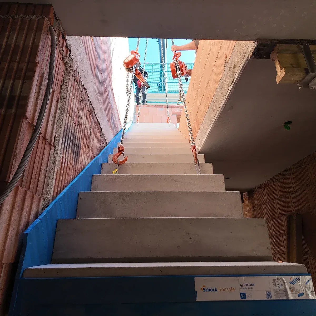 Treppe im Bau, Arbeiter darüber, blaues Sicherheitsnetz und Ziegelmauern auf beiden Seiten