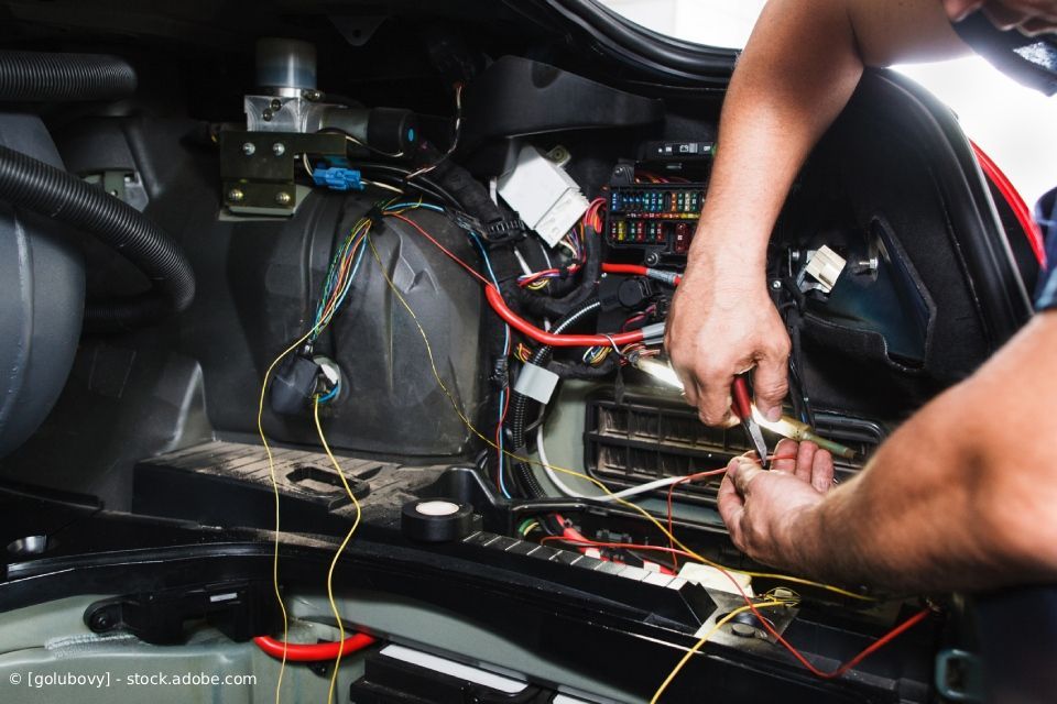 Ein Mechaniker arbeitet an der Elektrik im hinteren Fahrgastraum eines Fahrzeugs.