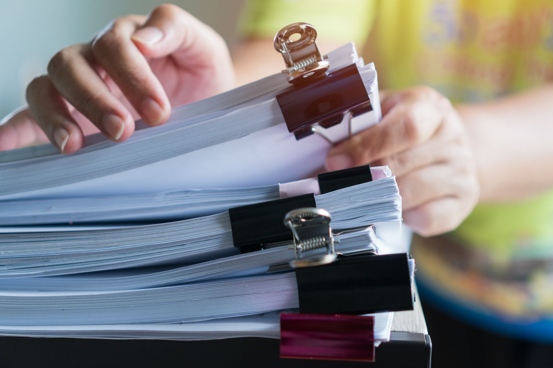 Personne tenant une pile de papiers fixés avec des trombones noirs et rouges.