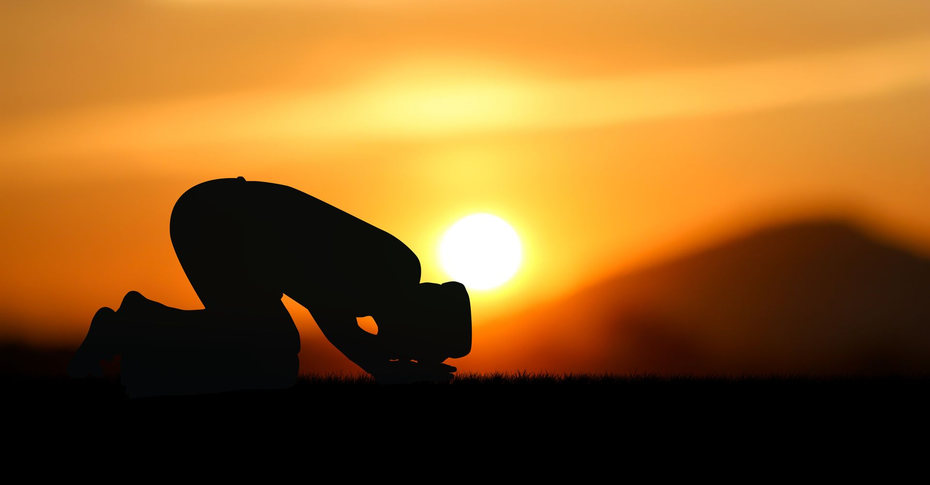 Silhouette d'une personne agenouillée en prière sur fond de soleil couchant.