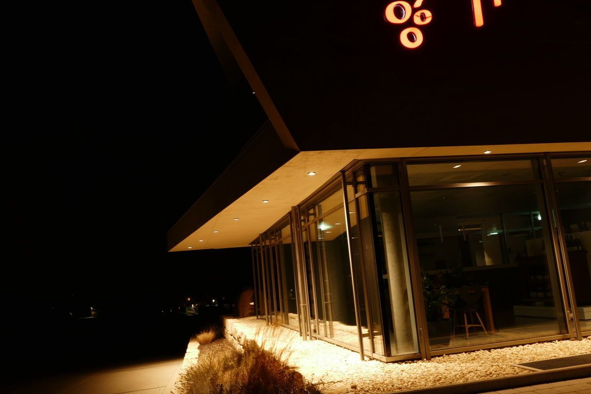 Außenansicht des Restaurants bei Nacht, beleuchtete Schilder über den Glasfenstern.