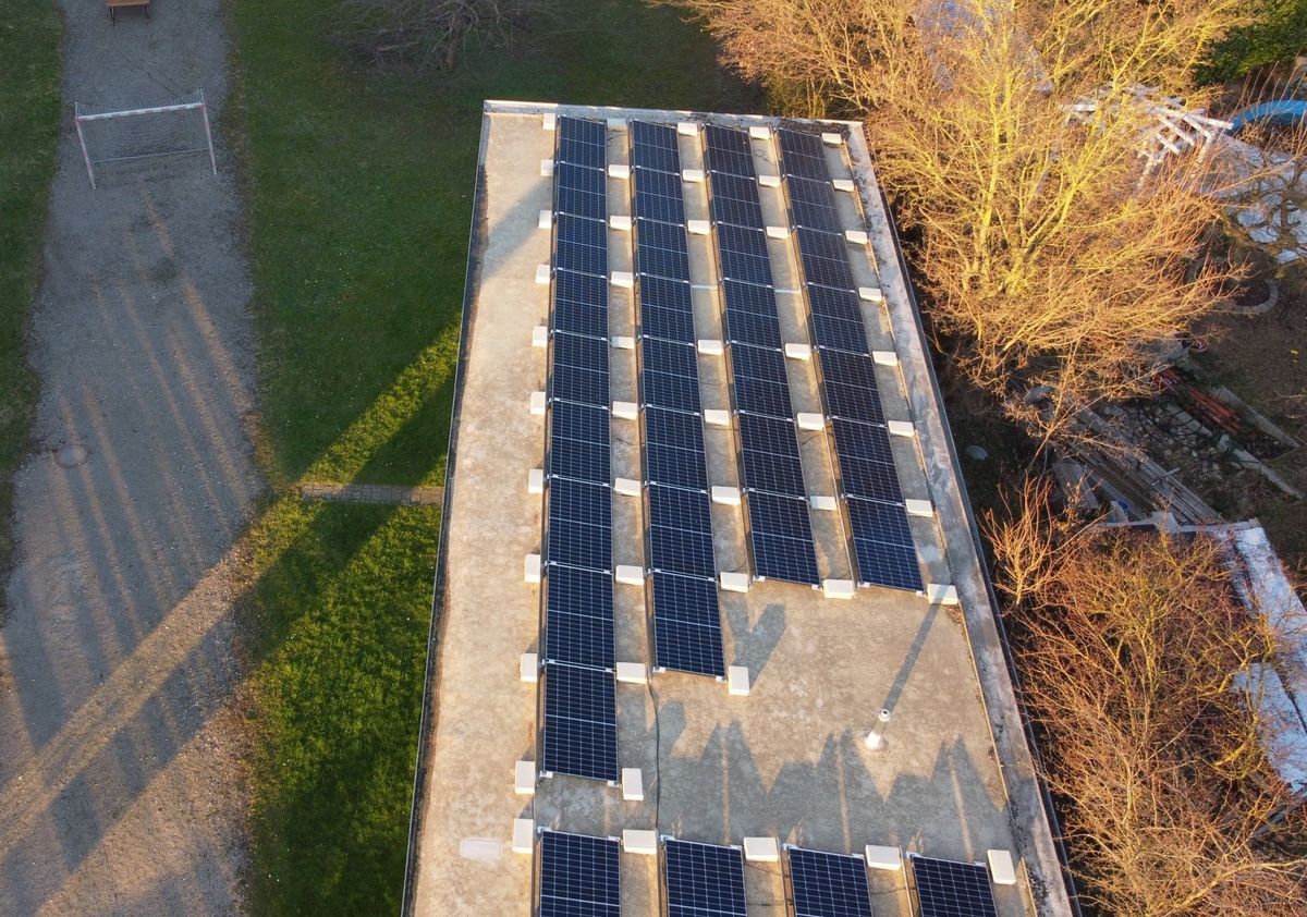 Solarpaneele auf dem Dach eines Gebäudes, daneben Gras und kahle Bäume.