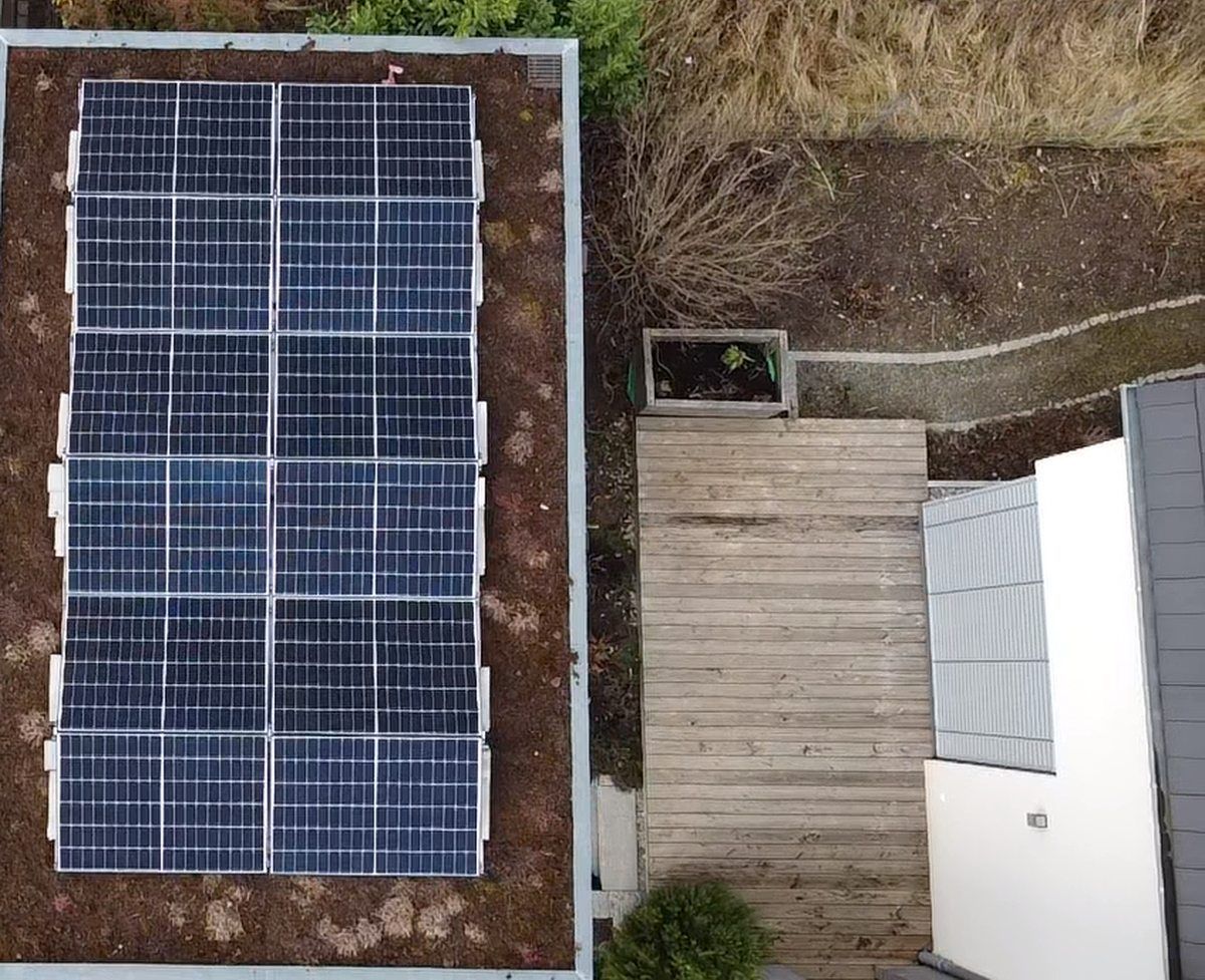 Draufsicht auf ein Dach mit Solarpaneelen, Gründach und Holzterrasse.