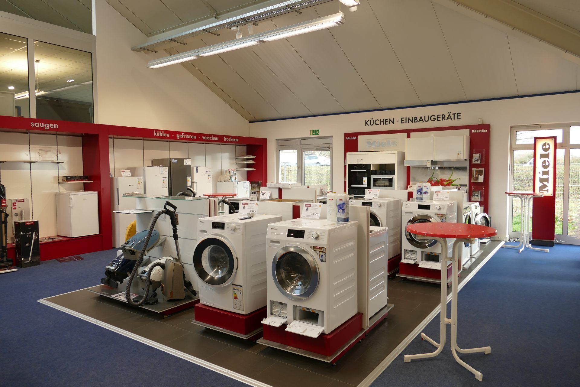 In einem Ausstellungsraum eines Geschäfts werden Haushaltsgeräte präsentiert, darunter Waschmaschinen, Backöfen