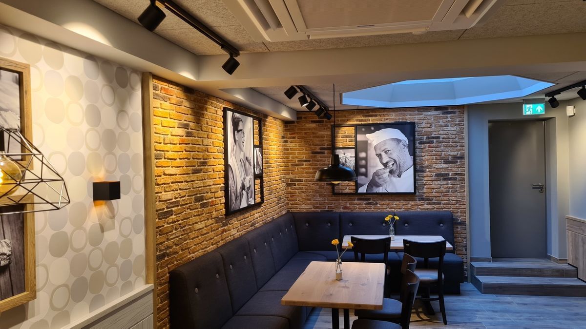 Restaurantinterieur mit Backsteinwand, Sitznischen, Schwarz-Weiß-Fotos und Schienenbeleuchtung.