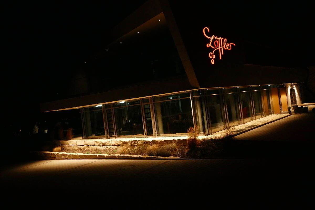 Außenansicht eines modernen Gebäudes bei Nacht, von unten beleuchtet. Ein Leuchtschild trägt die Aufschrift „Lippert“.