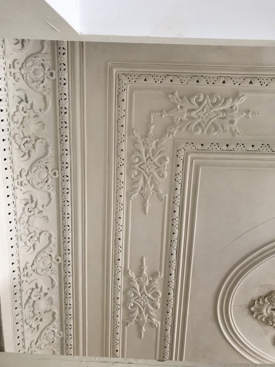 Close-up de um teto branco ornamentado com gesso floral e geométrico detalhado. Há um desenho circular.