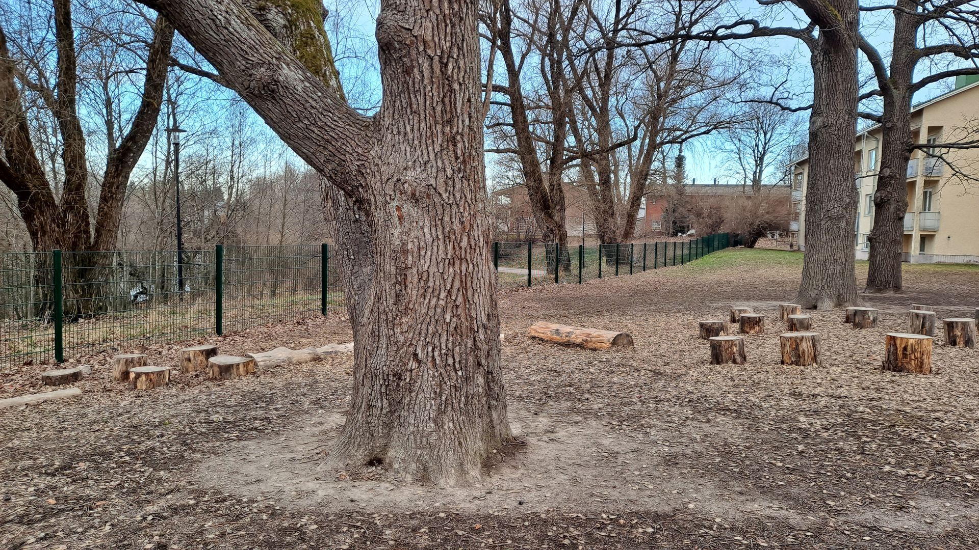 Worker in a hard hat and hi-vis vest inspecting a house foundation with exposed utility pipes.