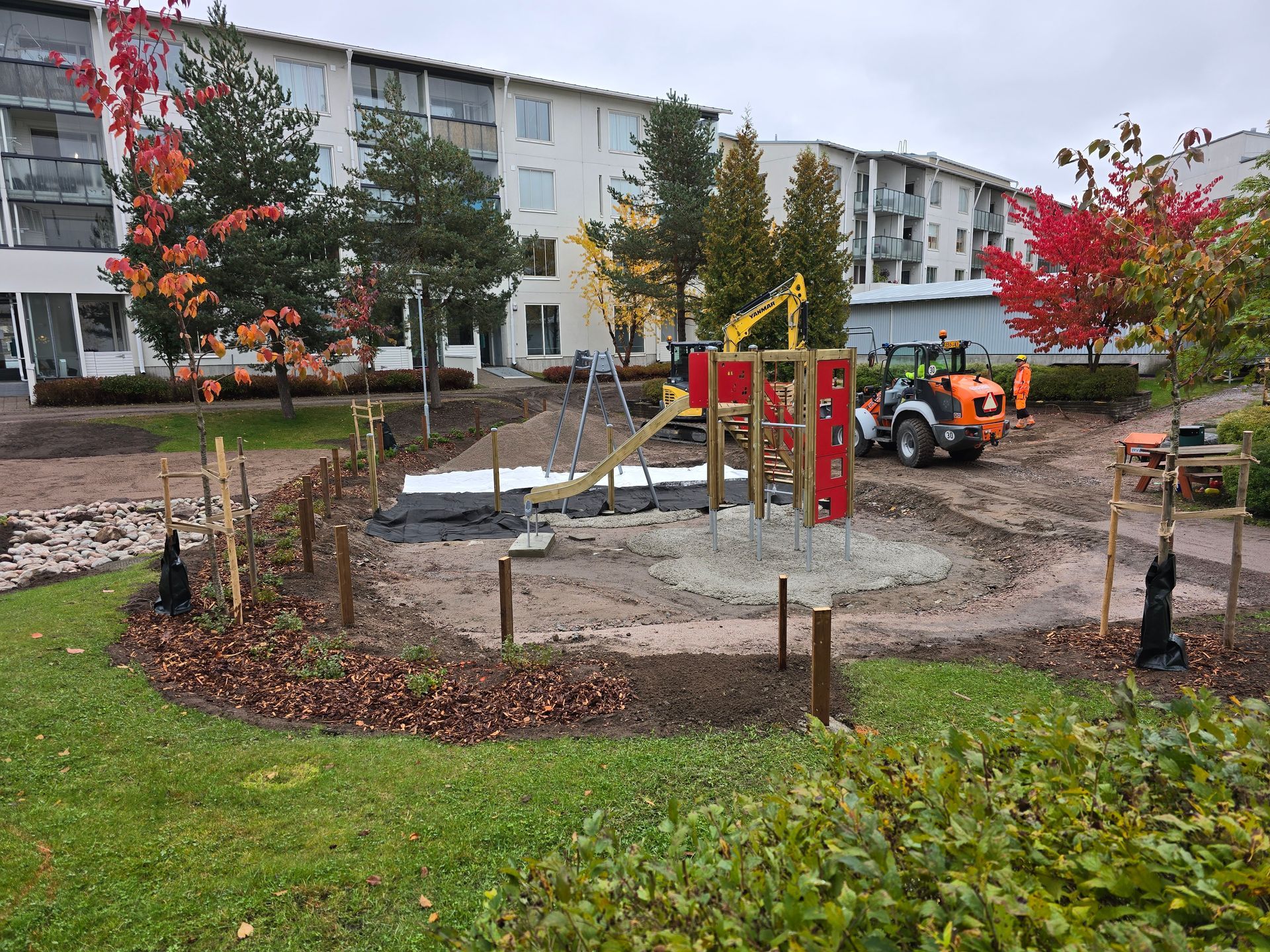Worker in a hard hat and hi-vis vest inspecting a house foundation with exposed utility pipes.