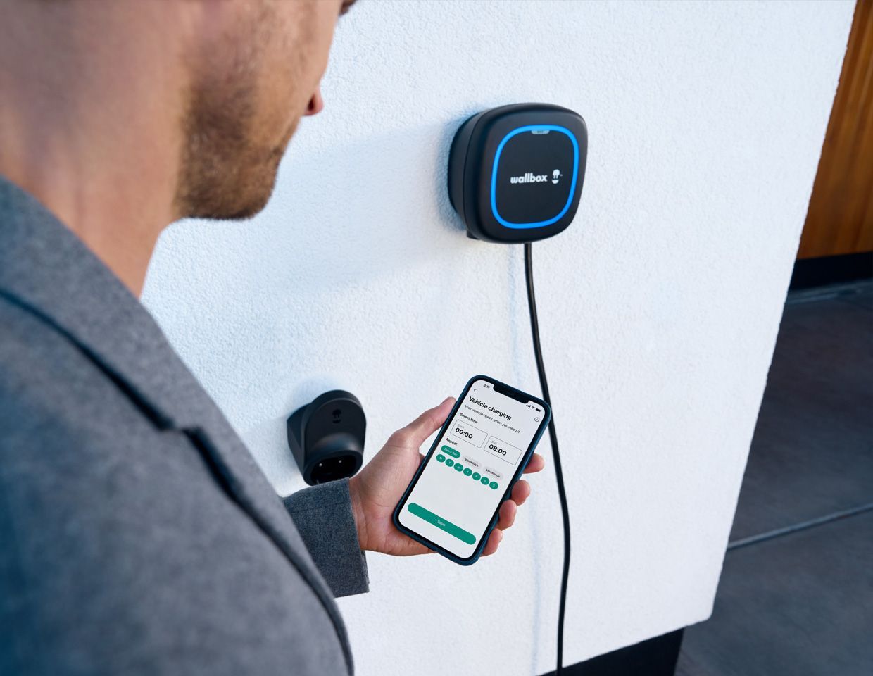 Une personne utilise un téléphone à côté d'un chargeur mural bleu avec un câble attaché.