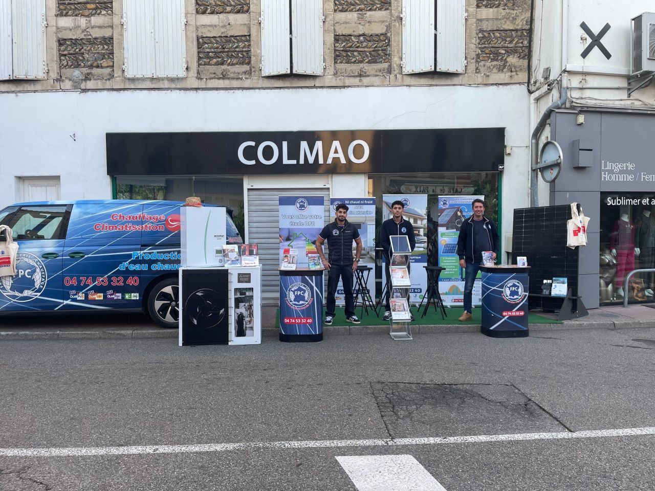 Scène de rue avec une devanture de magasin portant l'inscription COLMAO. Trois hommes se tiennent près de présentoirs publicitaires à l'extérieur. Une camionnette est garée à gauche.