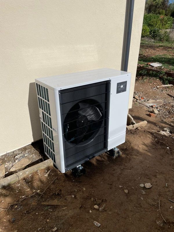 Unité de pompe à chaleur blanche avec ventilateur noir, montée sur la façade beige d'un bâtiment.
