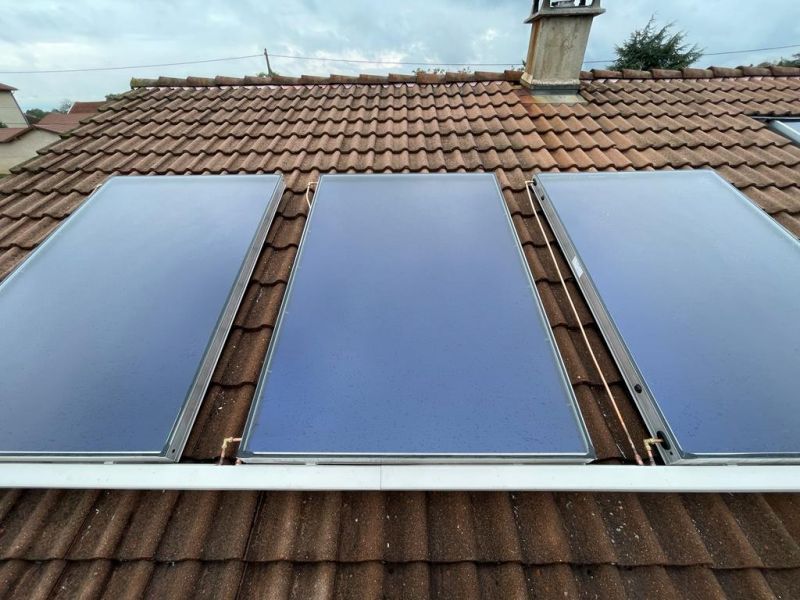 Trois panneaux solaires installés sur un toit de tuiles rouges, sur fond de ciel nuageux.