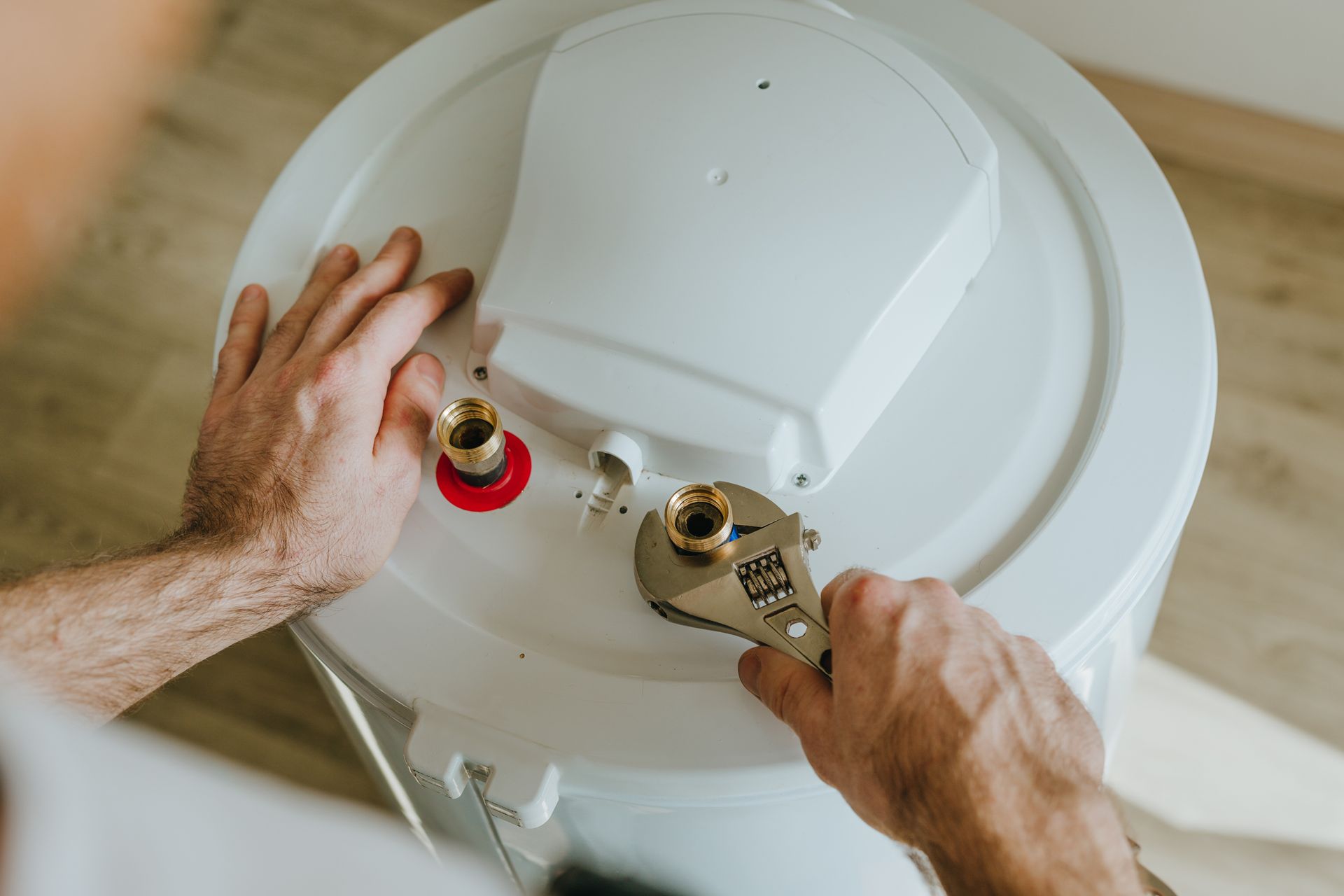 Personne utilisant une clé à molette pour travailler sur un chauffe-eau blanc, en intérieur.