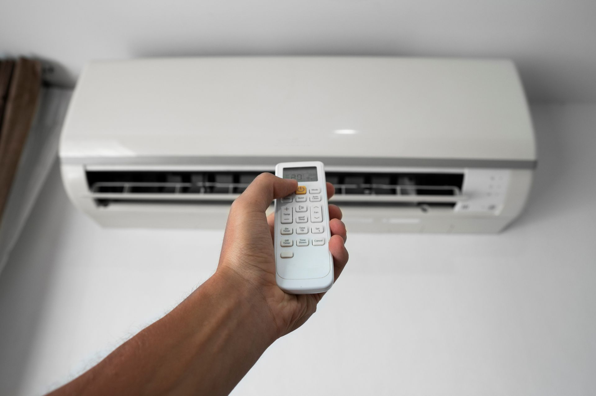 Une main tenant une télécommande blanche, pointant vers un climatiseur fixé sur un mur blanc.