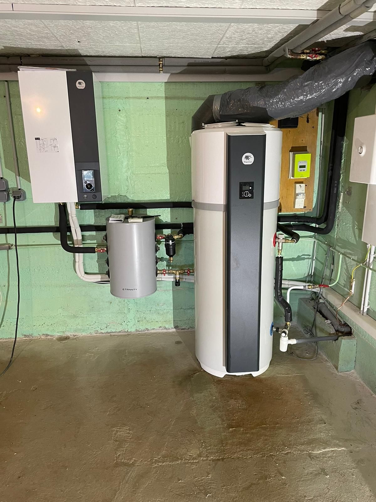 Local technique au sous-sol avec chauffe-eau, chaudière et équipements de plomberie sur sol en béton