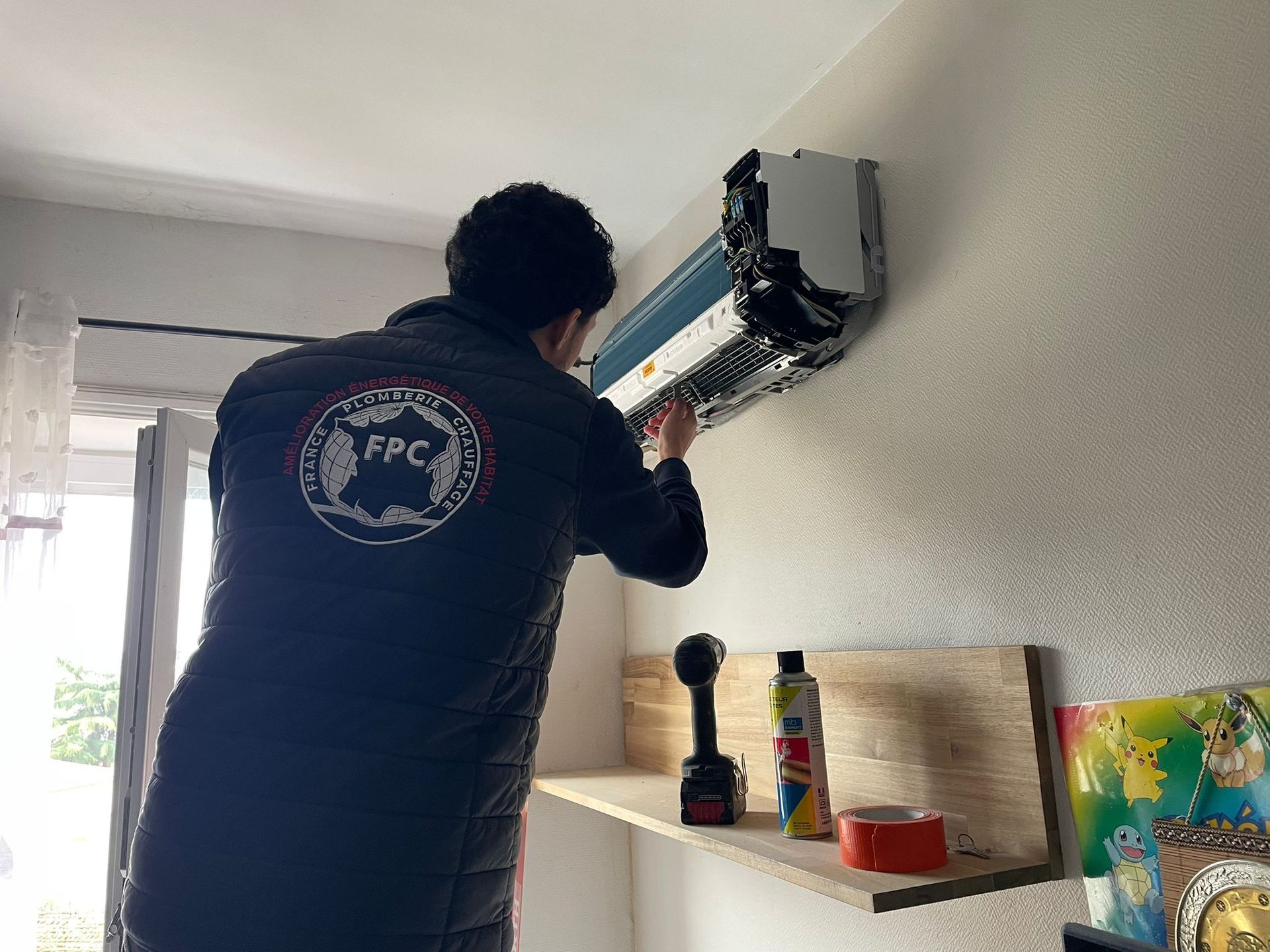 Un technicien installe un climatiseur mural à l'intérieur, ses outils à proximité.