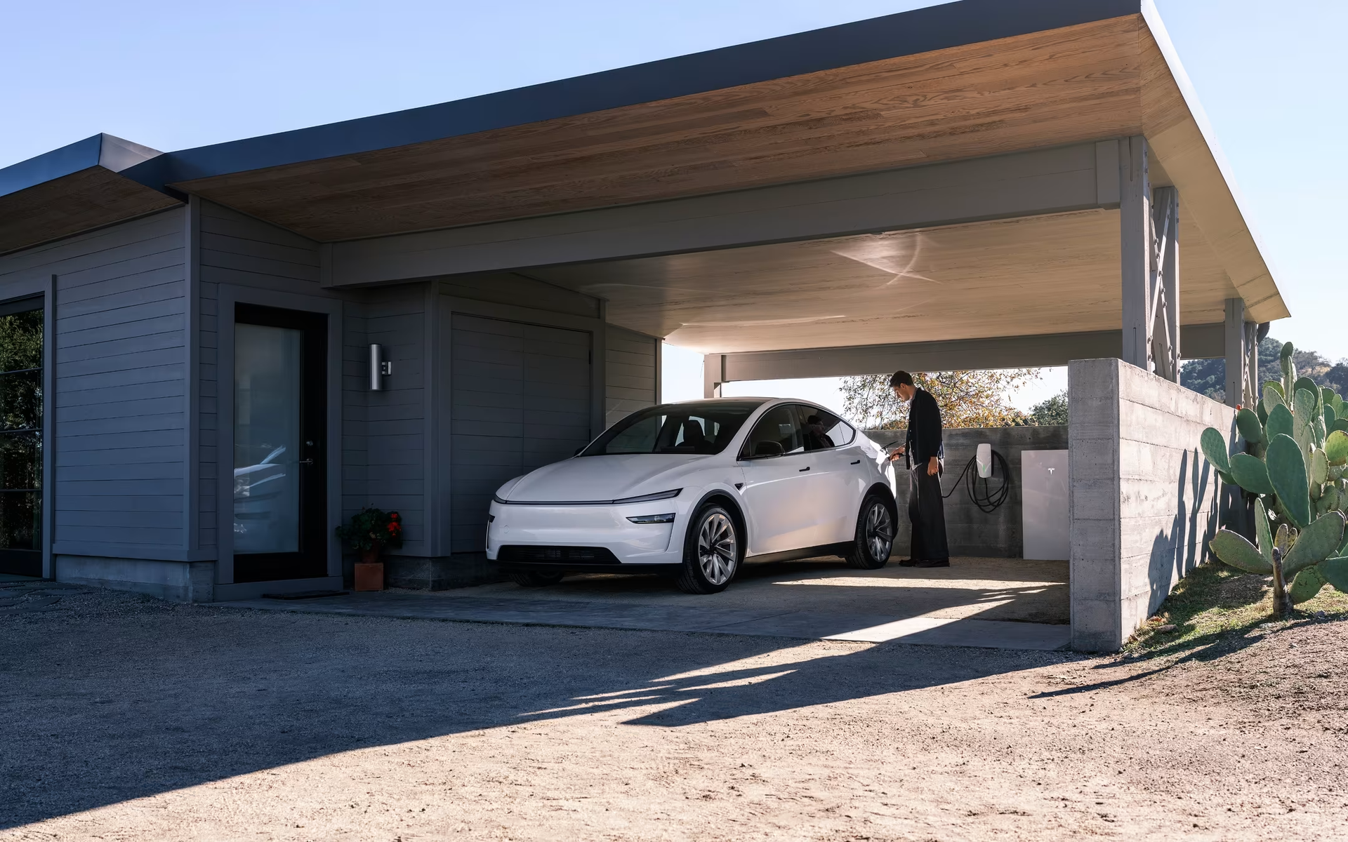 Voiture électrique blanche garée sous un abri ; une personne se tient près d'une borne de recharge.
