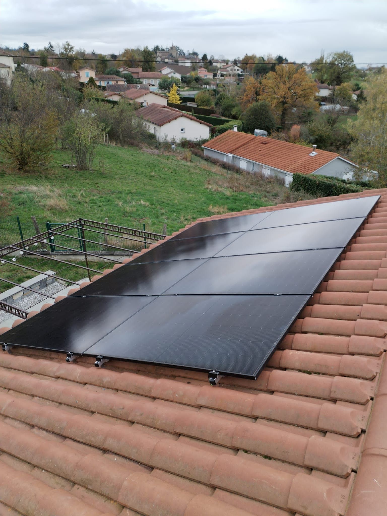 Des panneaux solaires sur un toit de tuiles rouges donnant sur un village et une colline verdoyante.