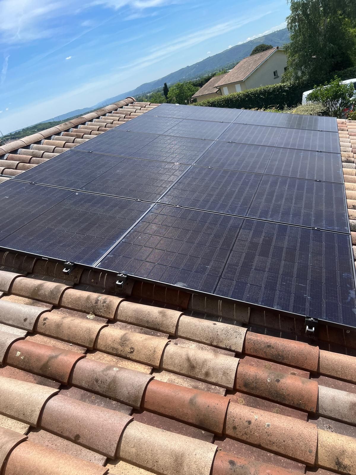 Des panneaux solaires installés sur un toit de tuiles sous un ciel bleu dégagé, avec des collines en arrière-plan.