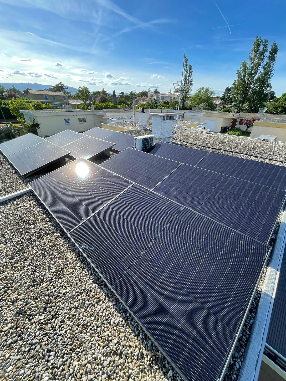 Des panneaux solaires sur un toit sous un ciel d'un bleu éclatant, avec du gravier et des arbres en arrière-plan.