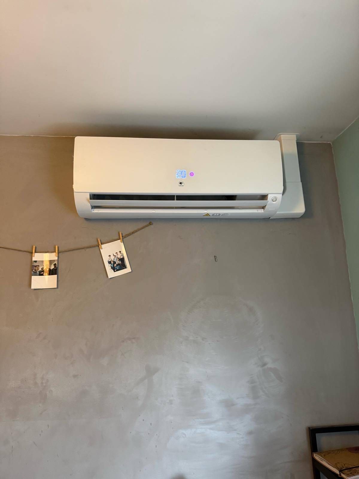 Mur blanc avec un climatiseur mural au-dessus d'une guirlande de petites photos accrochées au mur.
