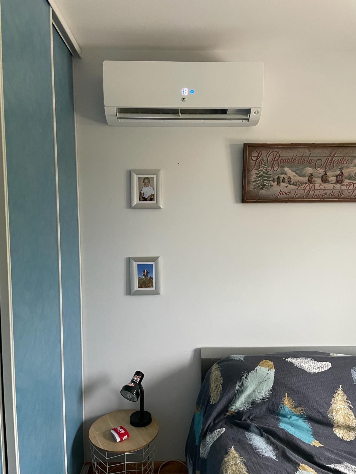 Mur de chambre avec climatiseur, tableau encadré, table de chevet et canapé à motifs à côté d'un rideau bleu