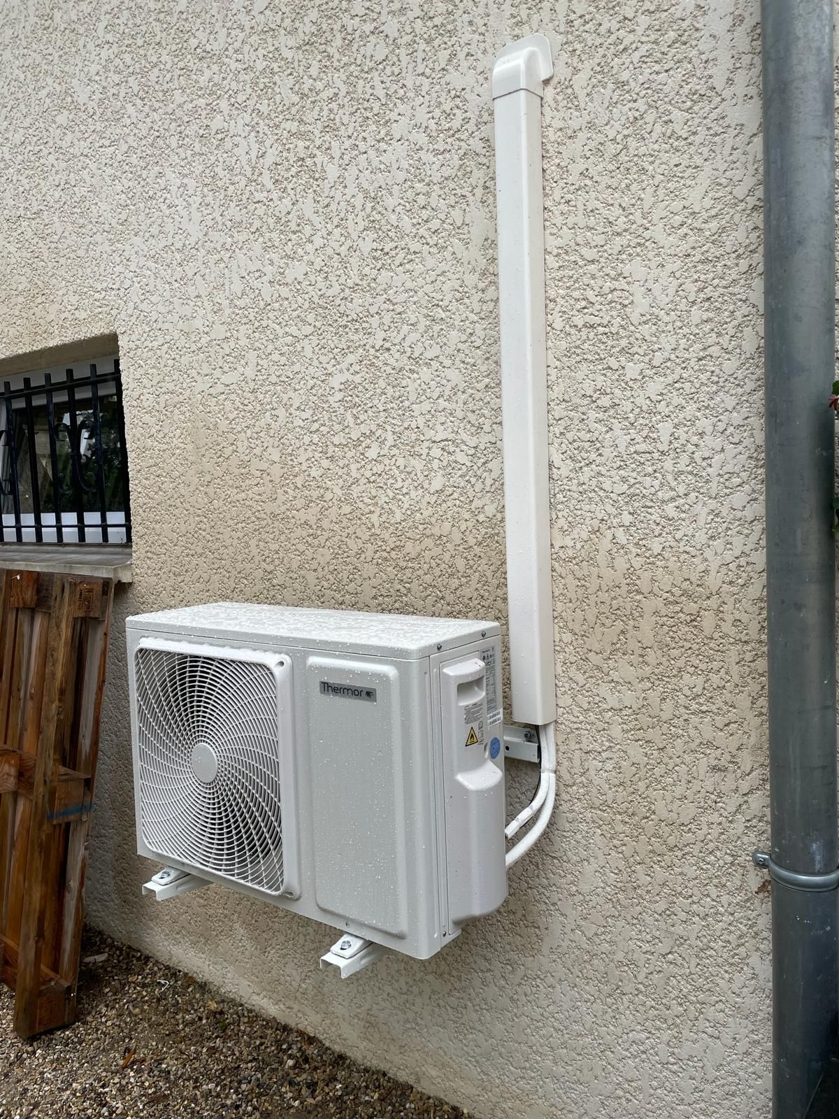 Unité de climatisation extérieure fixée sur un mur en stuc avec des conduits blancs