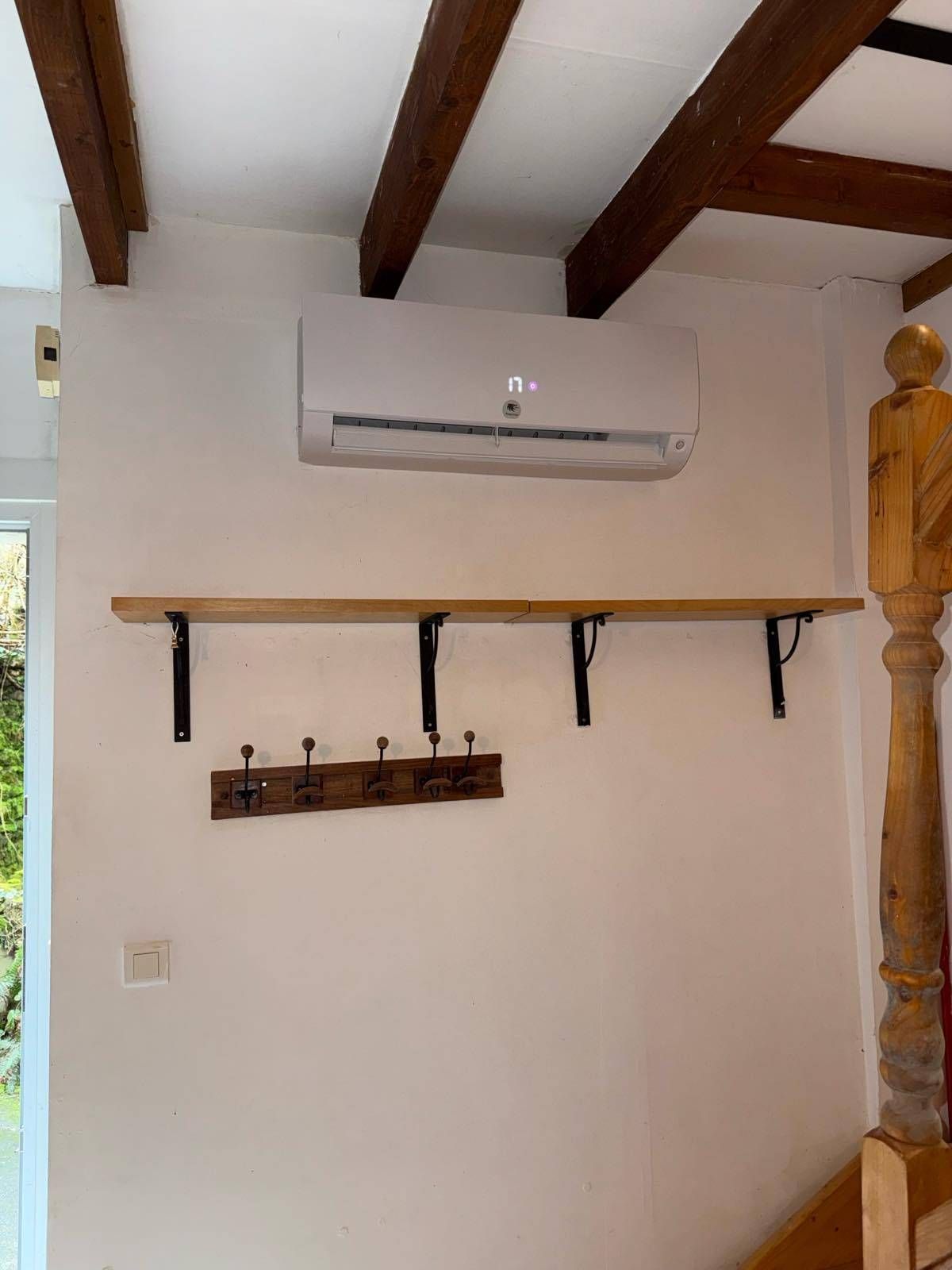 Mur intérieur avec climatiseur mural, étagère en bois, patères, poutres apparentes et partie de rampe d'escalier