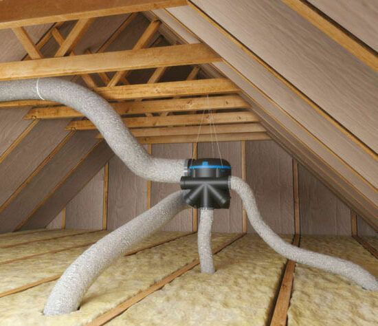 Grenier avec charpente apparente et isolation, montrant un ventilateur central et des conduits d'aération.