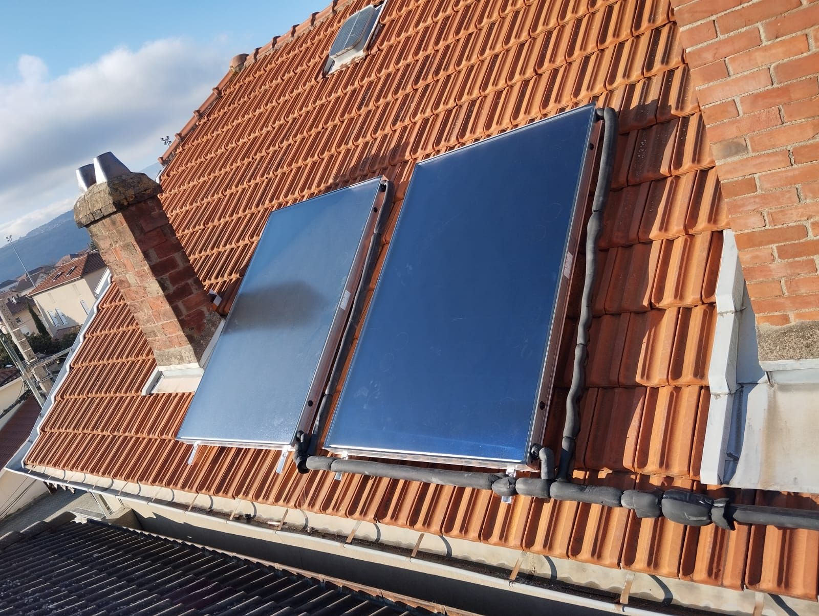 Deux panneaux solaires installés sur un toit de tuiles rouges sous un ciel bleu
