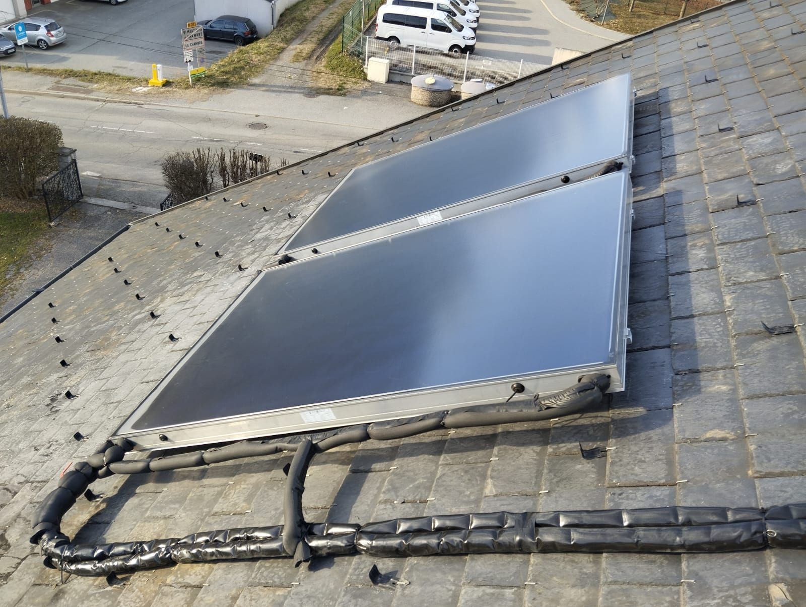 Panneaux solaires installés sur un toit en pente, avec câblage apparent et gravier sur le toit.