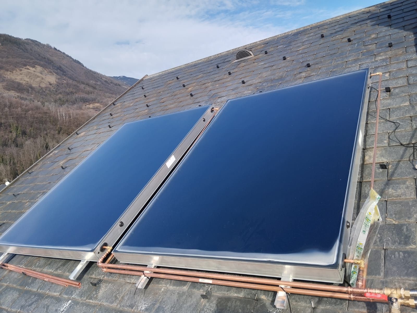Deux grands panneaux solaires bleus installés sur un toit avec des montagnes en arrière-plan