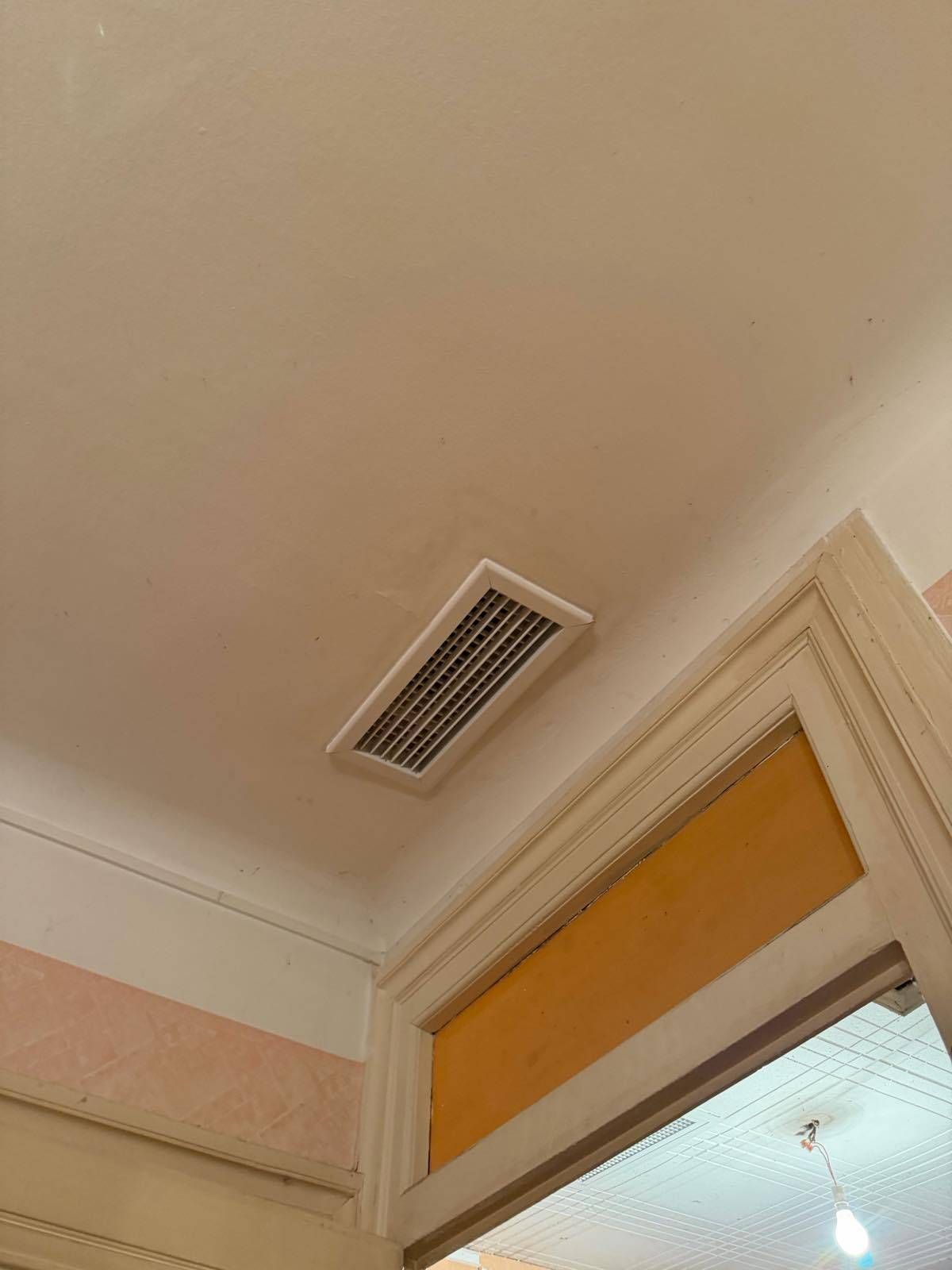 Grille d'aération au-dessus d'une porte avec store jaune et garniture crème