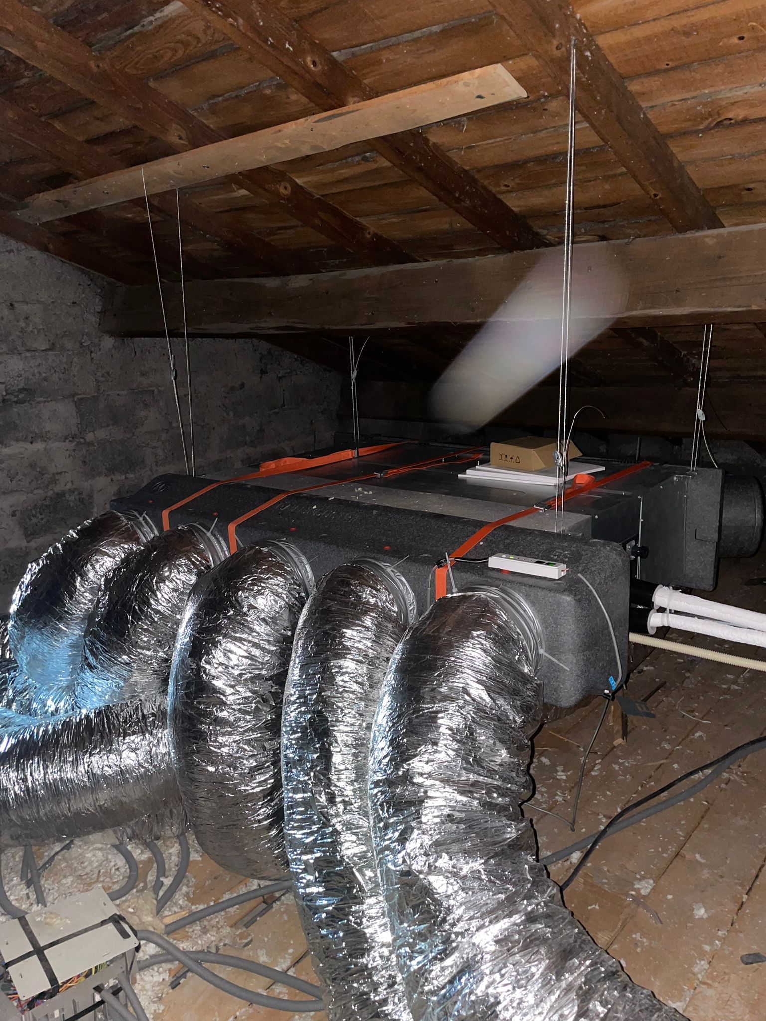 Conduits de chauffage, ventilation et climatisation isolés et grilles d'aération flexibles en argent dans un grenier sombre avec des poutres en bois apparentes.