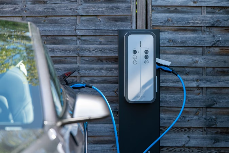 Borne de recharge pour véhicules électriques avec câbles bleus à côté d'une voiture garée et d'un mur en bois