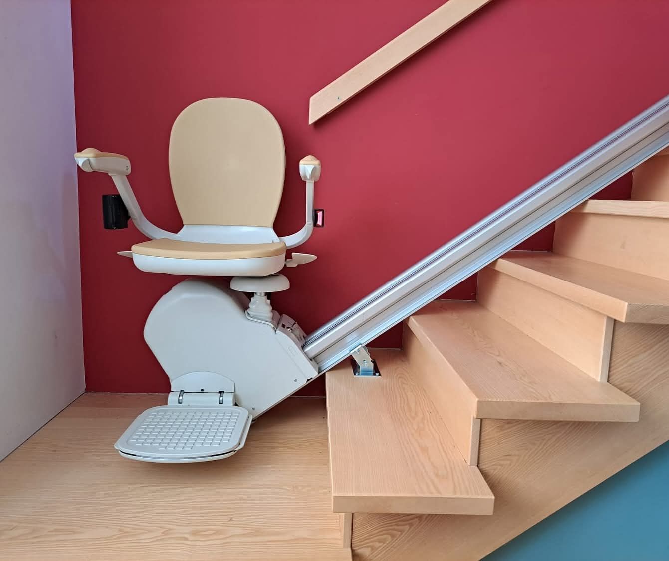 Fauteuil monte-escalier sur un escalier aux marches en bois et au mur rouge.