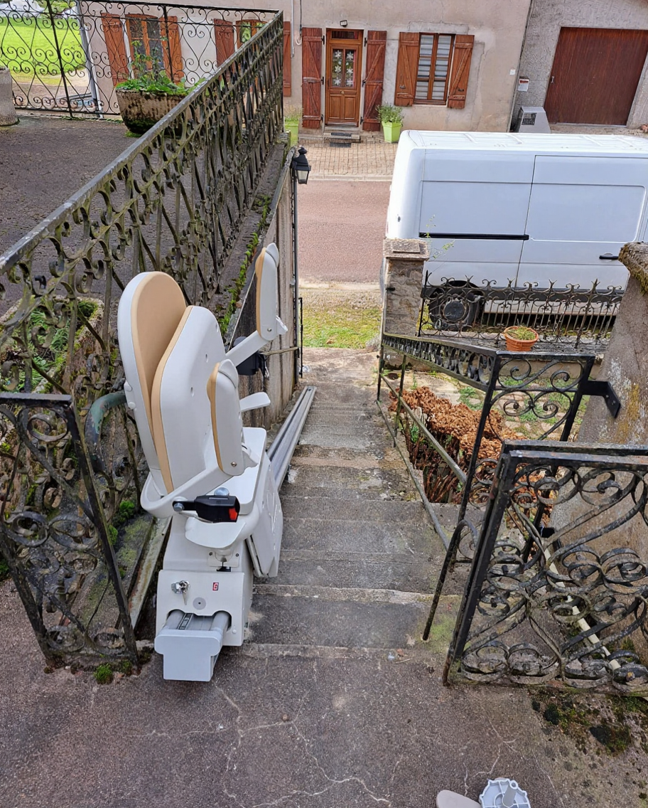 Monte-escalier blanc sur des marches extérieures en pierre, à côté d'une balustrade et d'un portail en fer forgé.